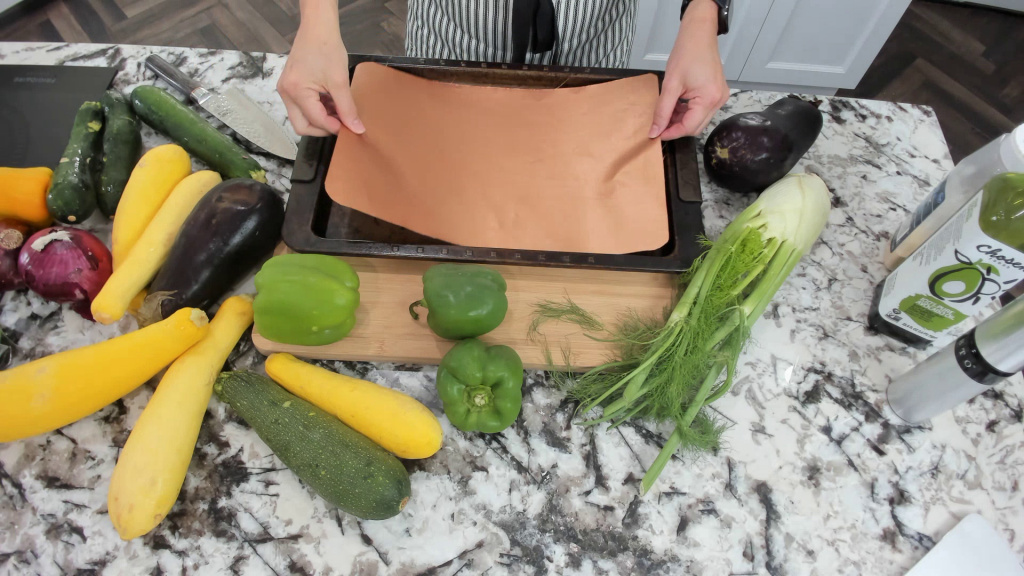 placing a grill mat onto a sheet pan with summer vegetables on a countertop