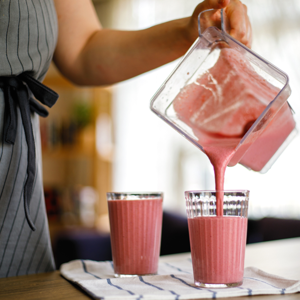 woman pouring a cherry almond smoothie from blender into glasses
