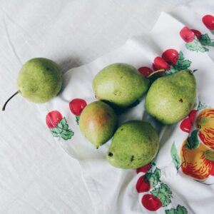 Green pears and one peach on a patterned cloth